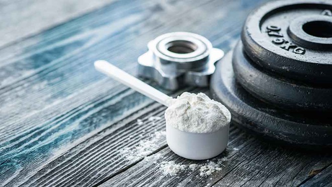 creatine in scoop with dumbell weights on table